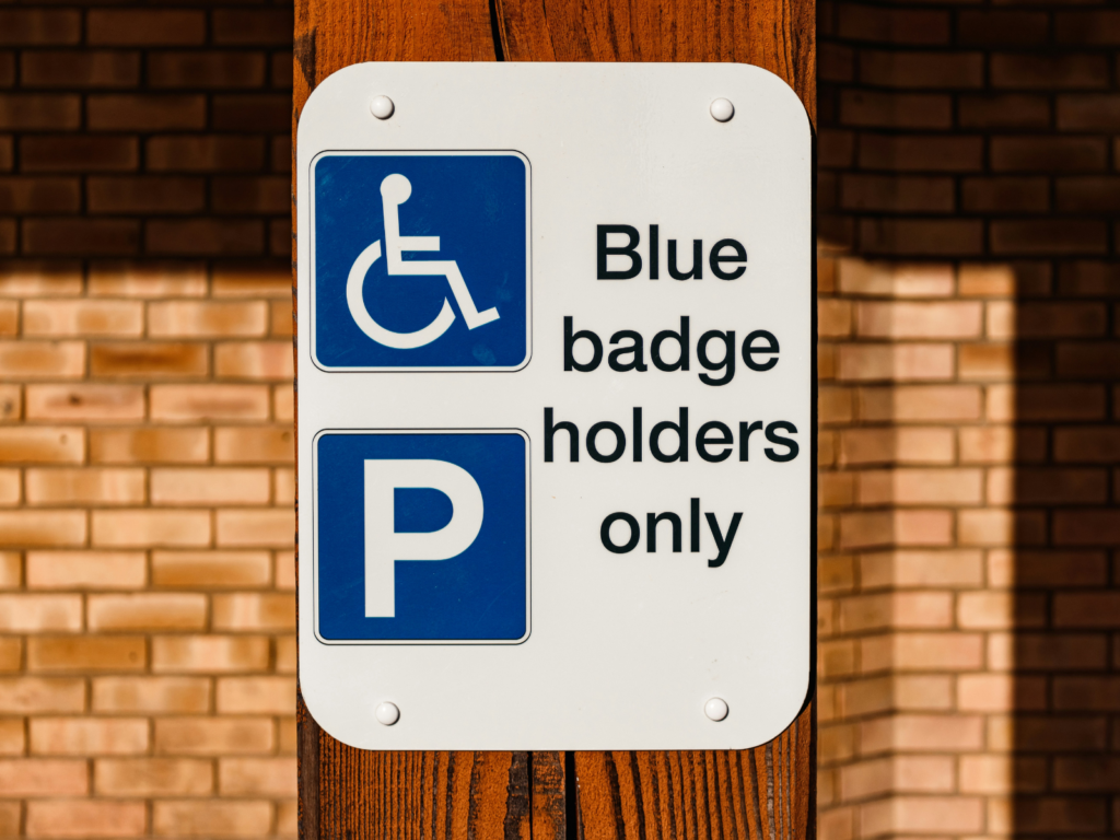'Blue Badge holders only' sign on wooden post, against brick wall, sunny day