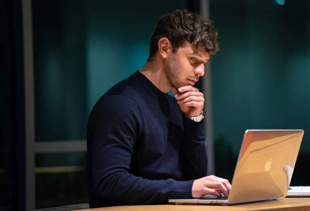 Man sat, thinking, while looking at laptop