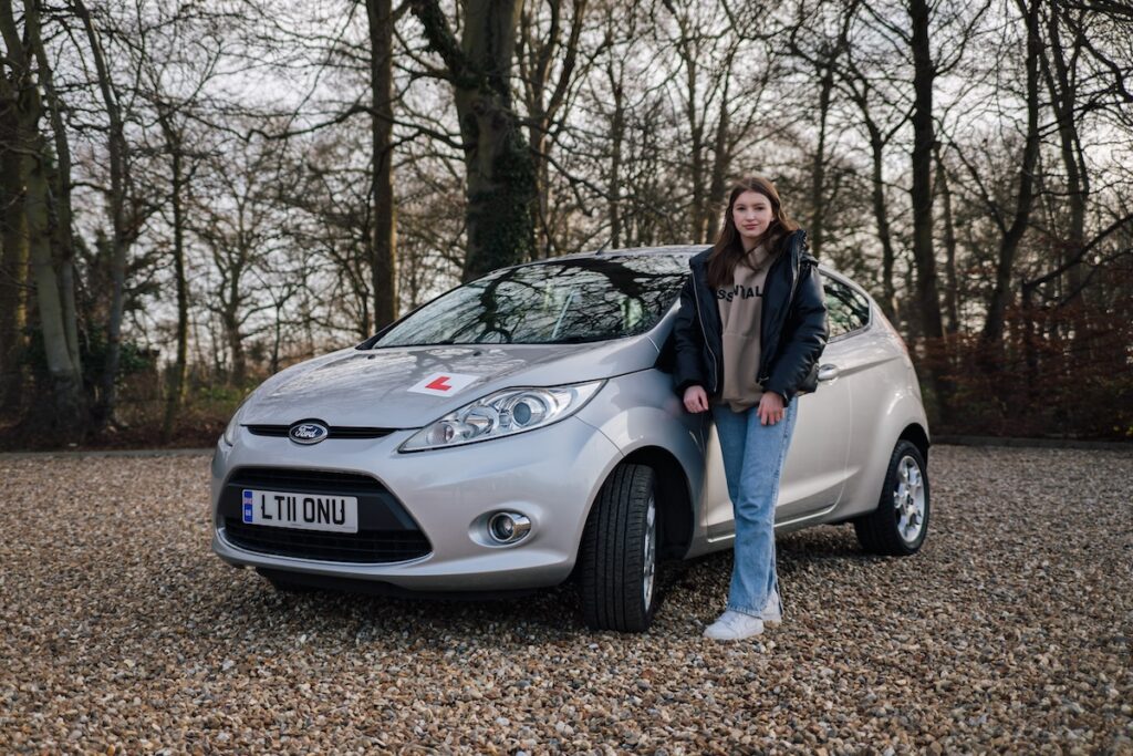 An image of someone standing next to a car with an 'L' plate on it